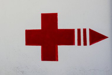 Okla işaretlenmiş kırmızı haç hastane kanadına yön gösteriyor, beyaz duvara işaret. Tıbbi hizmet kavramı, hastane yardımı.