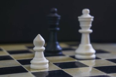 Küçük beyaz piyon satranç tahtasında siyah ve beyaz vezire karşı. Küçük parçanın önemi kavramı, takım çalışması, strateji, ebeveyn ve çocuk metaforu.