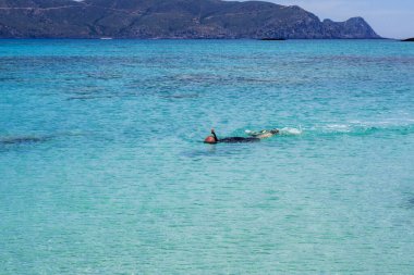 İnsanlar açık mavi deniz suyunda, adaların yakınında, resiflerde şnorkelle yüzerler..