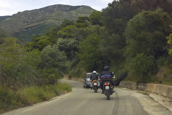 Two motorbikes following car before turning road in mountain area.