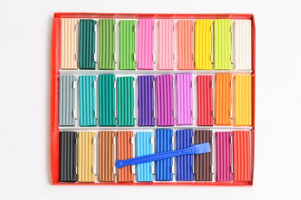 Multi-colored plasticine sticks in a cardboard box. Colorful plastic polymer clay set and sculptural knife on white background. — Stock Photo, Image