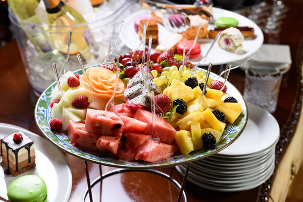 Sliced fruit on a plate with skewers and plates of sweets.