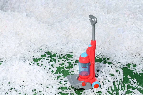 Children's toy plastic vacuum cleaner on green carpet with lots of paper white garbage — Stock Photo, Image