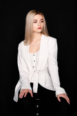 Sarı saçlı ve siyah elbiseli güzel genç mankenin yakın portresi, koyu arkaplanda fotostudio pozu.