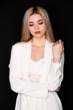 Sarı saçlı ve siyah elbiseli güzel genç mankenin yakın portresi, koyu arkaplanda fotostudio pozu.