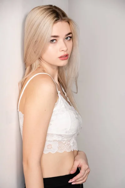 Beautiful young blonde girl posing in a white top on a light background — Stock Photo, Image