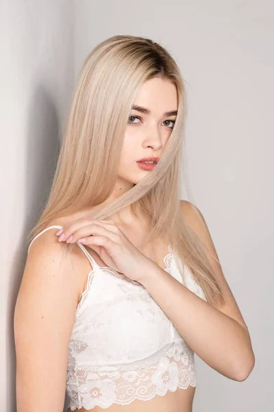 Beautiful young blonde girl posing in a white top on a light background — 스톡 사진