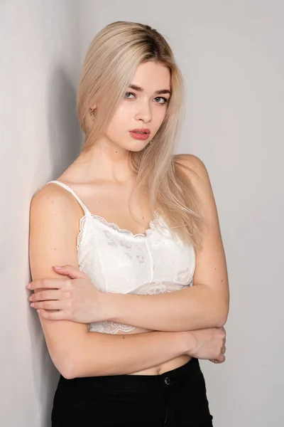 Beautiful young blonde girl posing in a white top on a light background — Stock Photo, Image