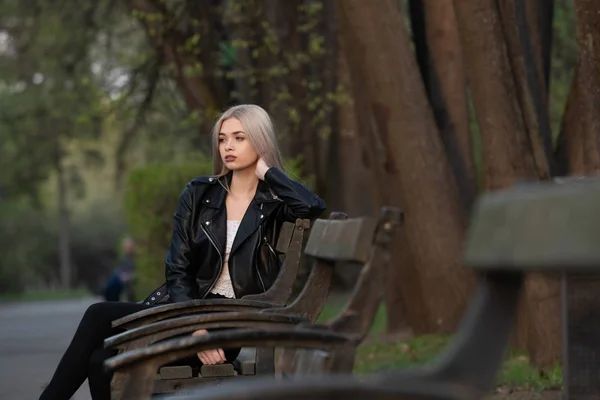 Krásná mladá blondýna dívka sedí na lavičce v parku — Stock fotografie