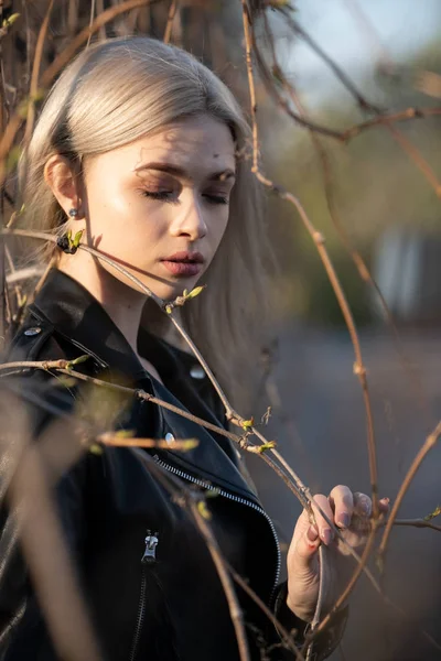 Młoda piękna blondynka pozuje wczesną wiosną obok gałęzi z zielonymi pączkami. Portret z bliska — Zdjęcie stockowe