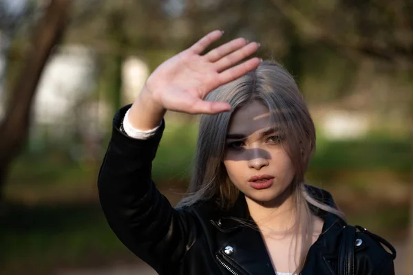 A beautiful young blonde girl holds her hand in front of her face hiding from the sun — 스톡 사진