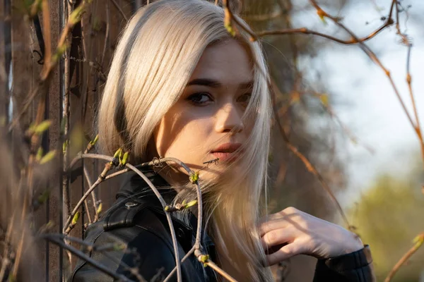 A young beautiful blonde girl poses next to branches with green buds in early spring. Close-up portrait — Stock Photo, Image