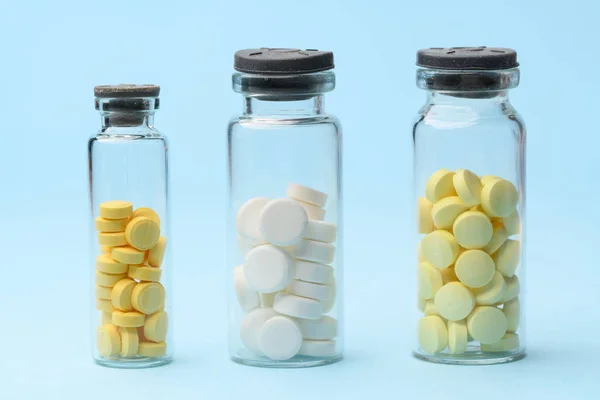 Gele en witte tabletten in glazen potten op een blauwe achtergrond — Stockfoto