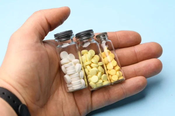 Een man houdt glazen potten met gele en witte tabletten op een blauwe achtergrond in de kamer — Stockfoto