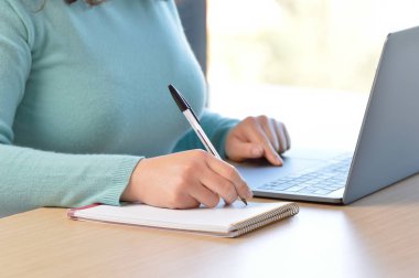 Ofiste dizüstü bilgisayarla not alan kadın elleri.