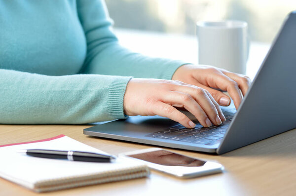 Cropped shot of a woman hands writing on a laptop at home