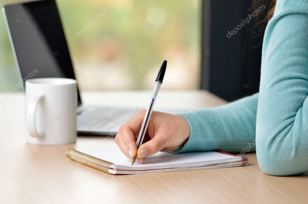 Female hand writing notes in a notebook on a desk at office