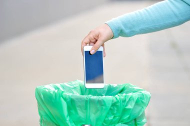Kırık ekranlı telefonu çöpe atarken çekilmiş bir el görüntüsü.