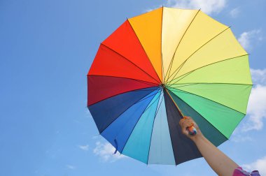 Güneşli gökyüzüne karşı çok renkli şemsiye tutan el