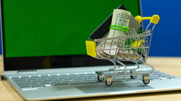 E-commerce shopping concept with miniature shopping cart and modern laptop.