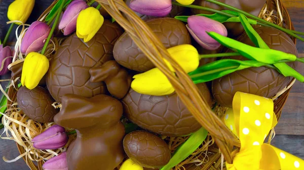 Счастливая пасхальная корзина с шоколадными яйцами и кроликами в большой корзине — стоковое фото