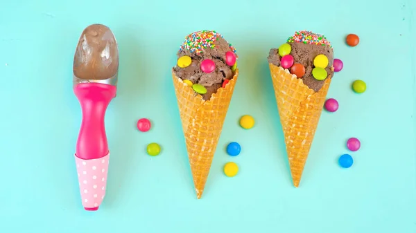 Chocolate ice cream cones decorated with candy, on blue wood overhead. — Stock Photo, Image