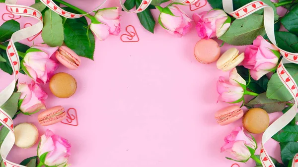 Moeders dag achtergrond van roze rozen en macaron koekjes op roze houten tafel. — Stockfoto
