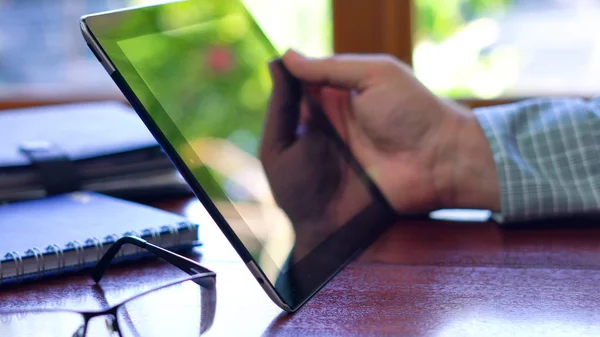 Man using tablet device closeup at desk in front of window.