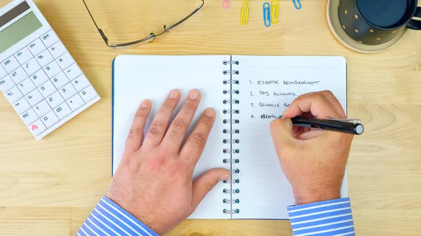 Empresario escribiendo lista de tareas pendientes en cuaderno, gastos generales . — Foto de Stock