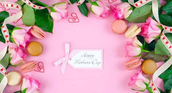 Mothers Day fondo de rosas rosadas y galletas macaron sobre mesa de madera rosada . — Foto de Stock