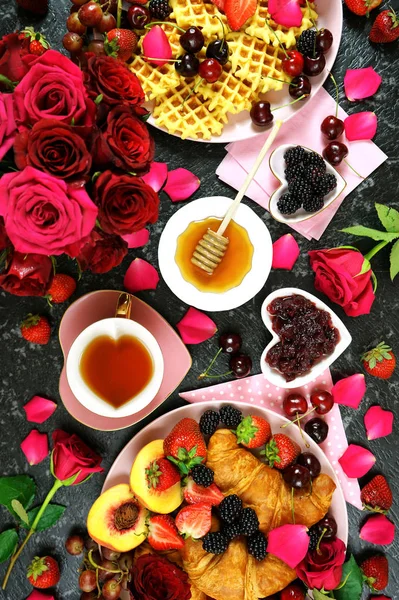 Romantisk överseende frukost med croissanter, pannkakor, våfflor frukt och rosor. — Stockfoto