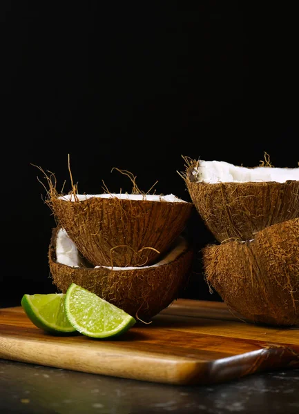 Coconut halves and limes spotlighted against a black background.