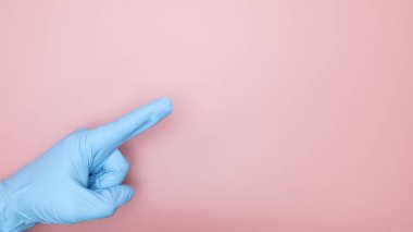 Doktor eli mavi eldivenli pembe arka planda izole edilmiş parmak işareti kopyası alan