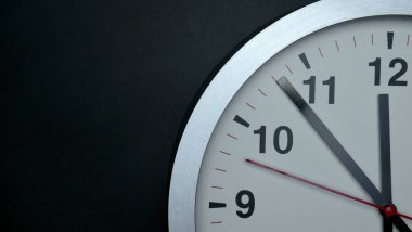 Saat 12 yönünde. Siyah zemin üzerinde beyaz duvar saati. Geceyarısına 100 saniye var..