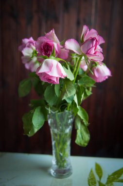 Pembe güller karanlık bir arka planda vazoda soluyor.