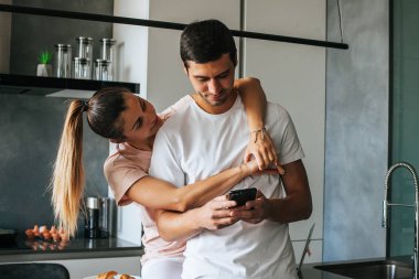 Güzel, mutlu, genç bir çift kahvaltıda akıllı telefon kullanıyor.