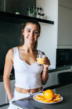 Genç atletik kız sabahın köründe taze portakal suyu içer.