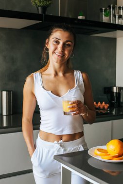 Genç atletik kız sabahın köründe taze portakal suyu içer.