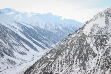 Karla kaplı bir dağda dolambaçlı bir yolun uzak görünümü. Otobanın drone atışı.