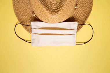 Yaz 2020 konsepti: sade sarı arka planda hasır şapka ve maske. Coronovirus covid tatil gezisi.