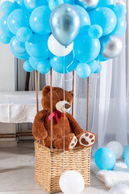 Büyük oyuncak ayı mavi balonlu balon sepetinde. Çocuklar kapalı bir sepette otururken oyuncak ayı gibi kızarır. Çocukların doğum günü süslemesi