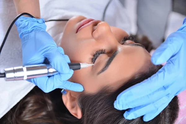 Permanent makeup eyeliner procedure, applying on a beautiful young girl in a beauty studio with a tattoo instrument. Beauty treatment and permanent makeup concept. Close up, selective focus