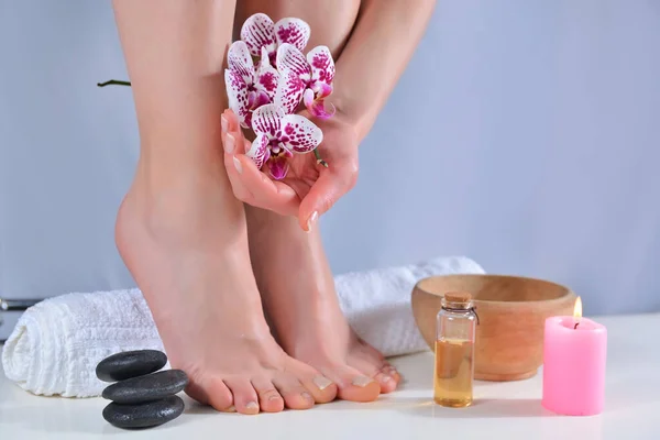 Female feet and hands with natural polish color manicure and pedicure on a towel and purple orchid. Bowl and candles in background in beauty salon. Spa and pedicure concept. Close up, selective focus