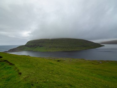 Faroe Adaları. Leitisvatn Gölü, Tralanpan manzaralı. Ön planda yeşil çimenler var. Puslu bir manzara. Geniş açı.