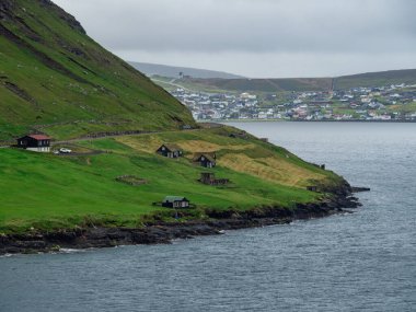 Faroe Adaları. Tepeler ve yeşil çayırlar. Arka planda Sorvagur kasabası. Bulanık manzara.