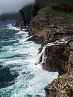 Faroe Adaları, Vagar, Basdalafossur şelaleleri. Şelalenin ve okyanusun üzerindeki kayalıkların manzarası. Haşin manzara.