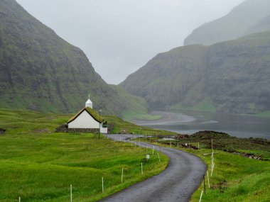 Faroe Adaları, Streymoy, Saksun. Saksun 'un kilisesine ve vadisine bakın. Çimen çatılı beyaz bina yeşil alanların dışında duruyor..