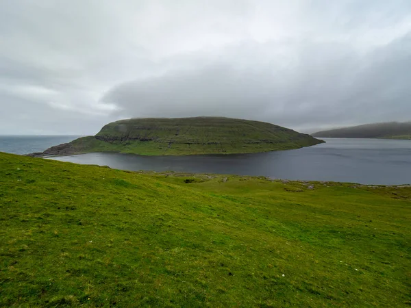 Faroe Adaları. Leitisvatn Gölü, Tralanpan manzaralı. Ön planda yeşil çimenler var. Puslu bir manzara. Geniş açı.
