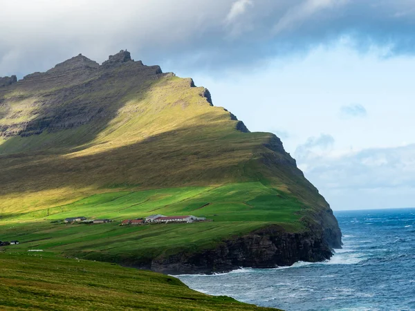 Faroe Adaları, Vidoy, Vidaredii. Uçurumların ve köyün üzerindeki yeşil tepelerin muhteşem manzarası. Mavi gökyüzü biraz bulutlu.