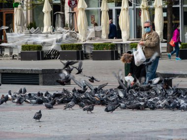 Krakow / Polonya - 22 / 04 / 2020. Krakow 'un ana meydanında covid-19 koronavirüs salgını sırasında güvercin beslemek. Turist yok, halk maskeli..